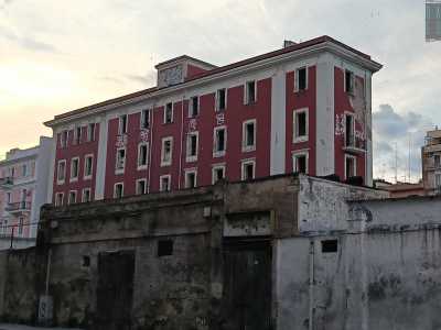 L�edificio, dall�ampia e rossa facciata scrostata, si innalza su cinque livelli scanditi da una lunga serie di finestre parallele, divise da due fasce bianche verticali che corrono lungo tutto il prospetto